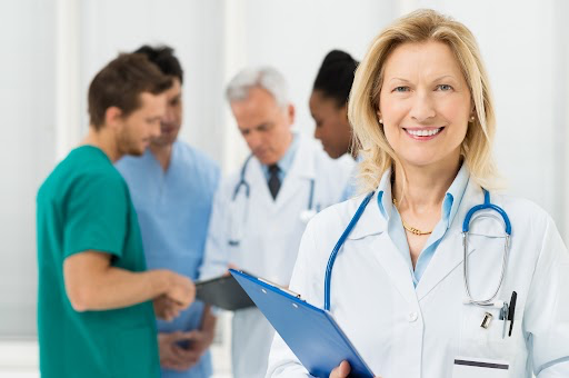 Smiling female doctor holding clipboard in urgent care center with medical team in background – healthcare marketing and SEO for small business concept.