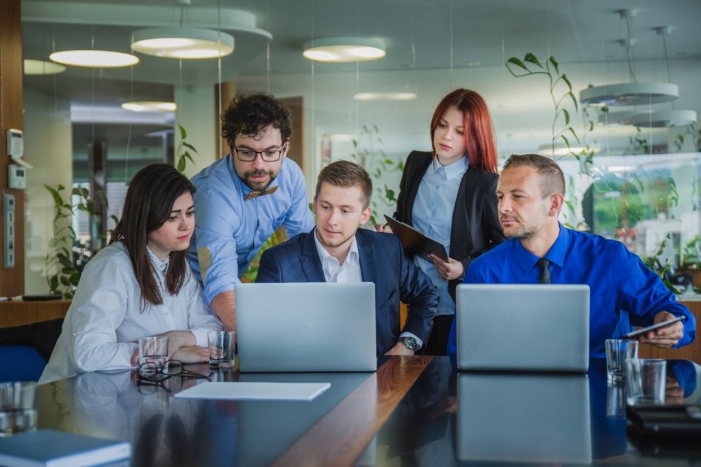 Five people gathered around a laptop as one person presents, illustrating teamwork and digital marketing for small businesses.

