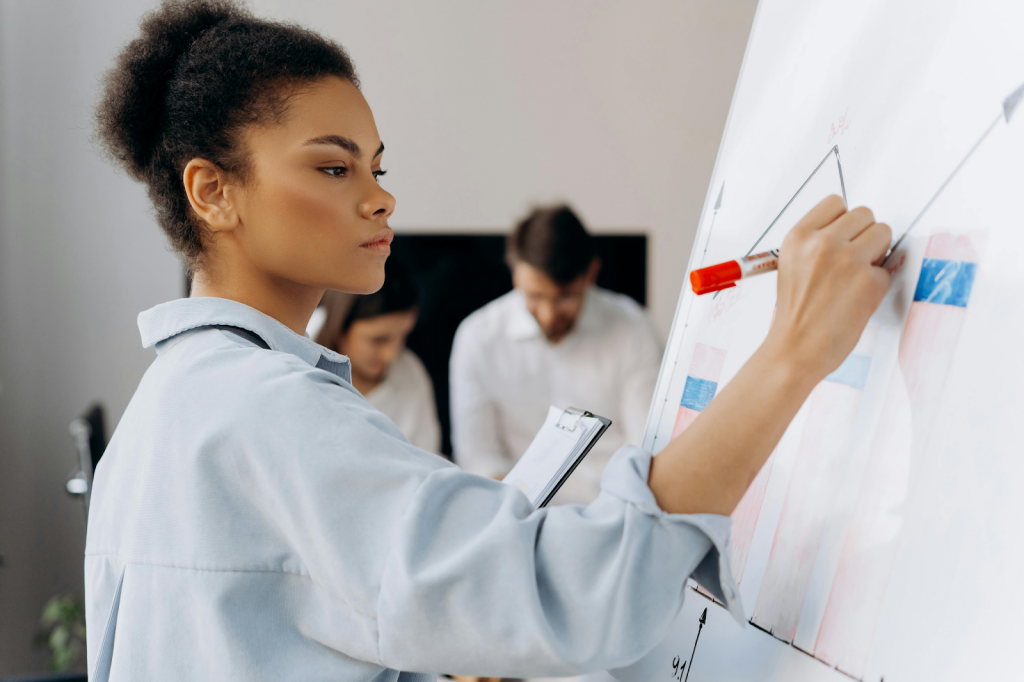 Woman presenting a growth strategy on a whiteboard for B2B SEO companies while colleagues discuss in the background
