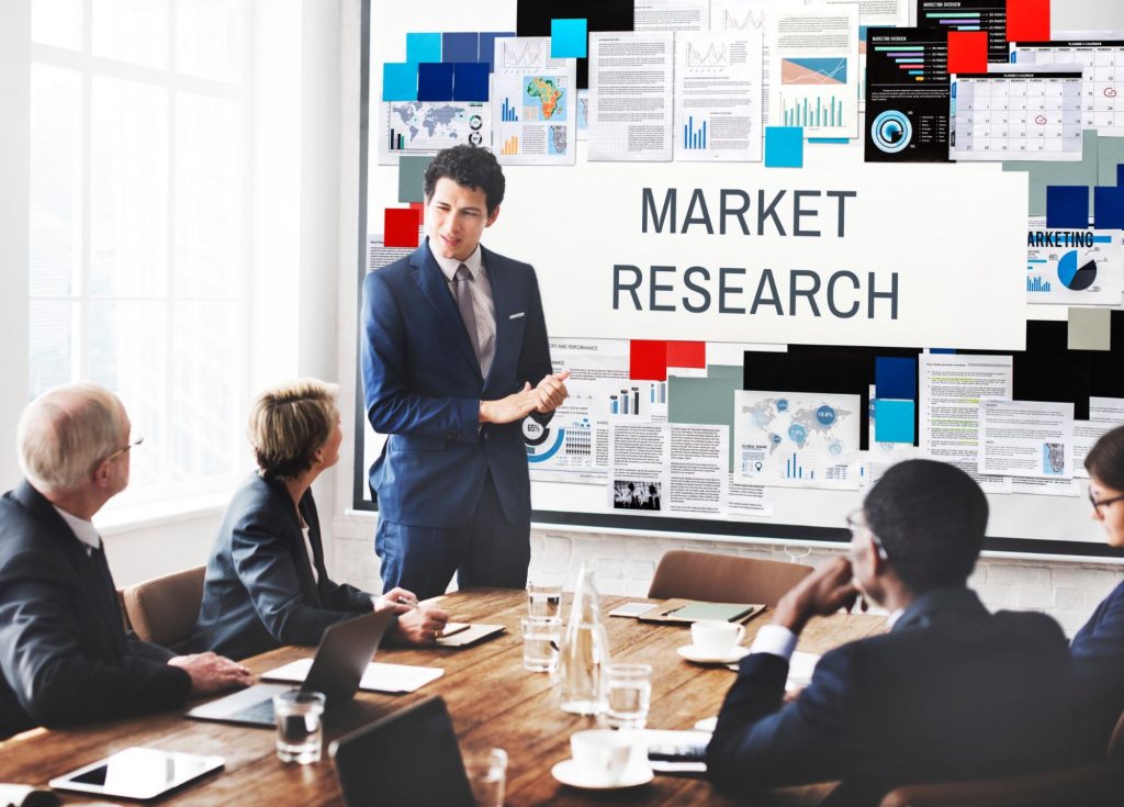 Team leader discussing market research with teammates around a table, big screen showing components, highlighting marketing services for startups.

