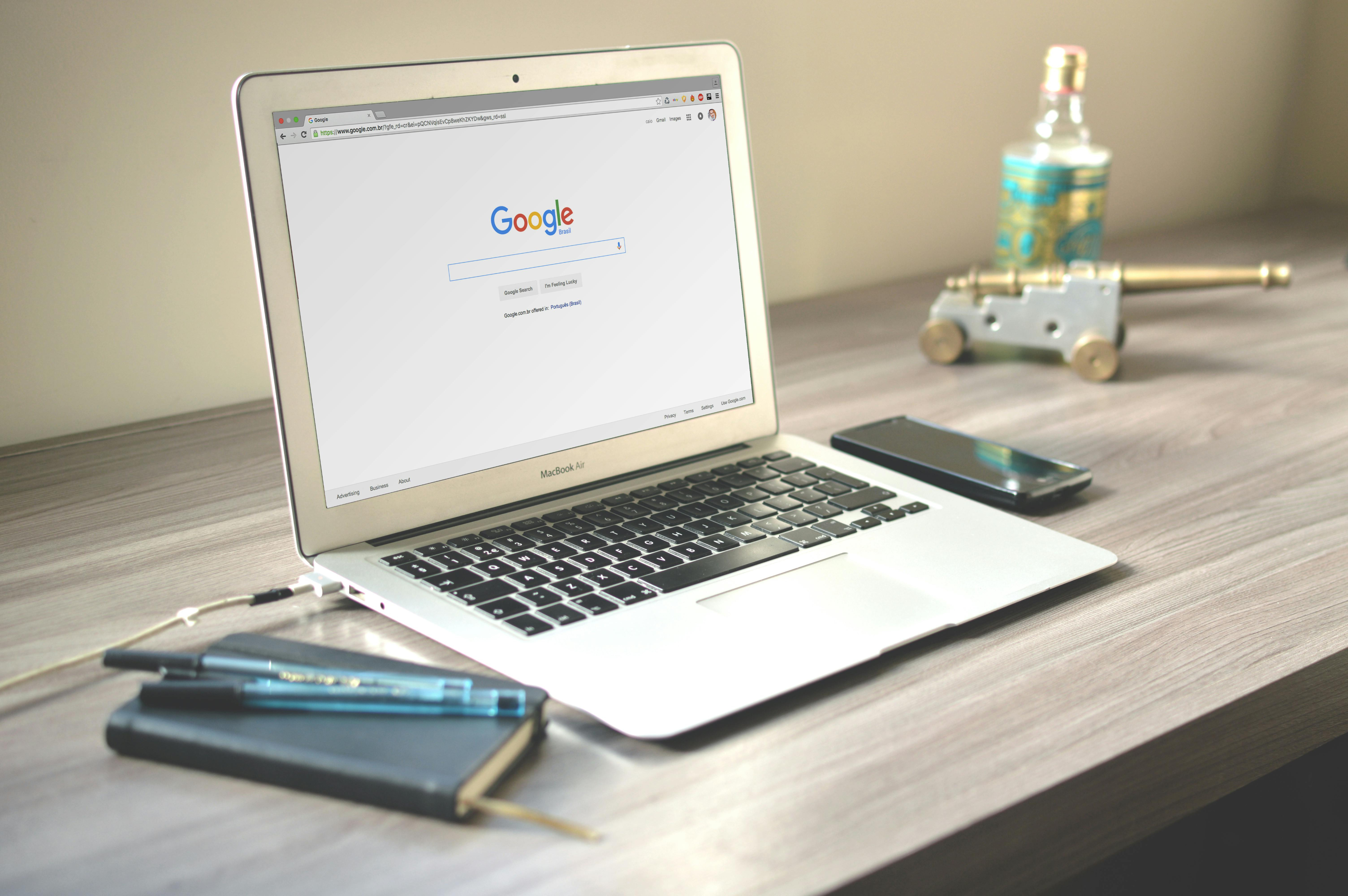 Laptop with Google open, notebook, and phone on table, representing affordable SEO services for small businesses improving online visibility.