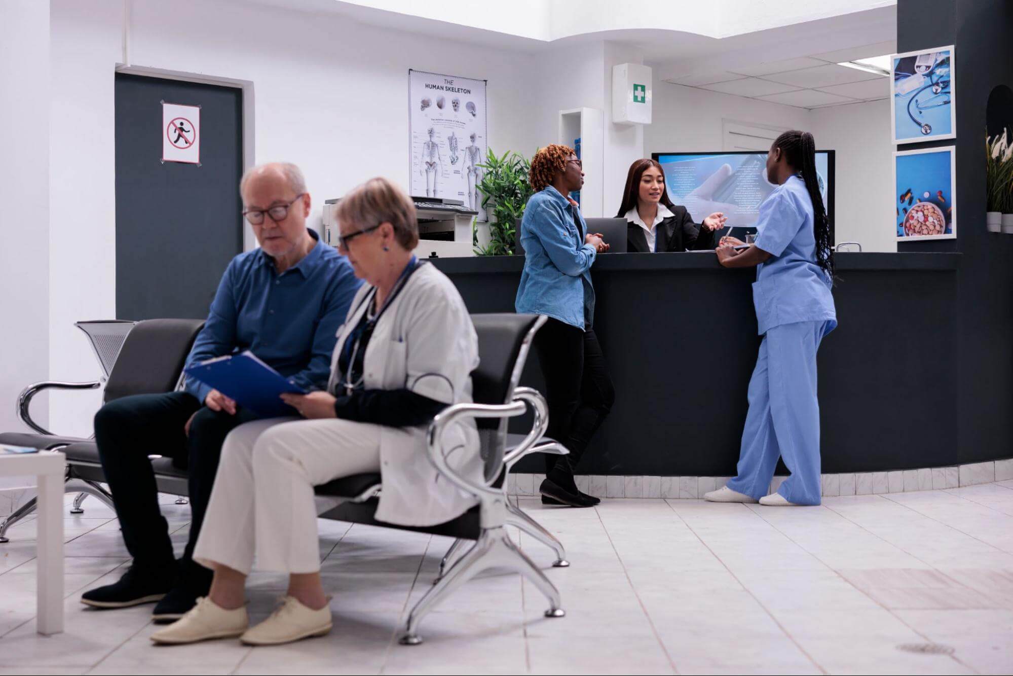 A lady doctor explains care details to an elderly patient while two nurses speak to the receptionist—showcasing improved clinic flow with urgent care SEO.