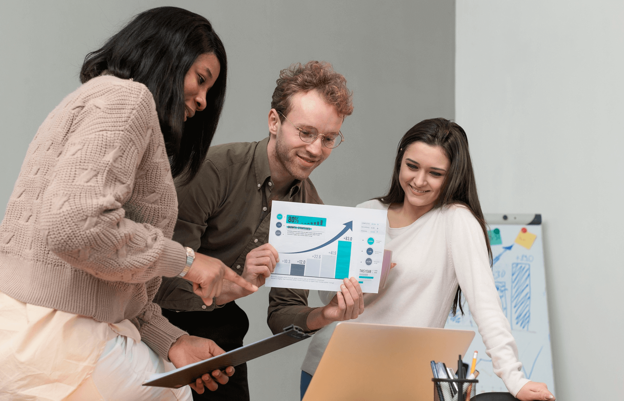 Three people engaged in a discussion while reviewing a chart on a laptop.