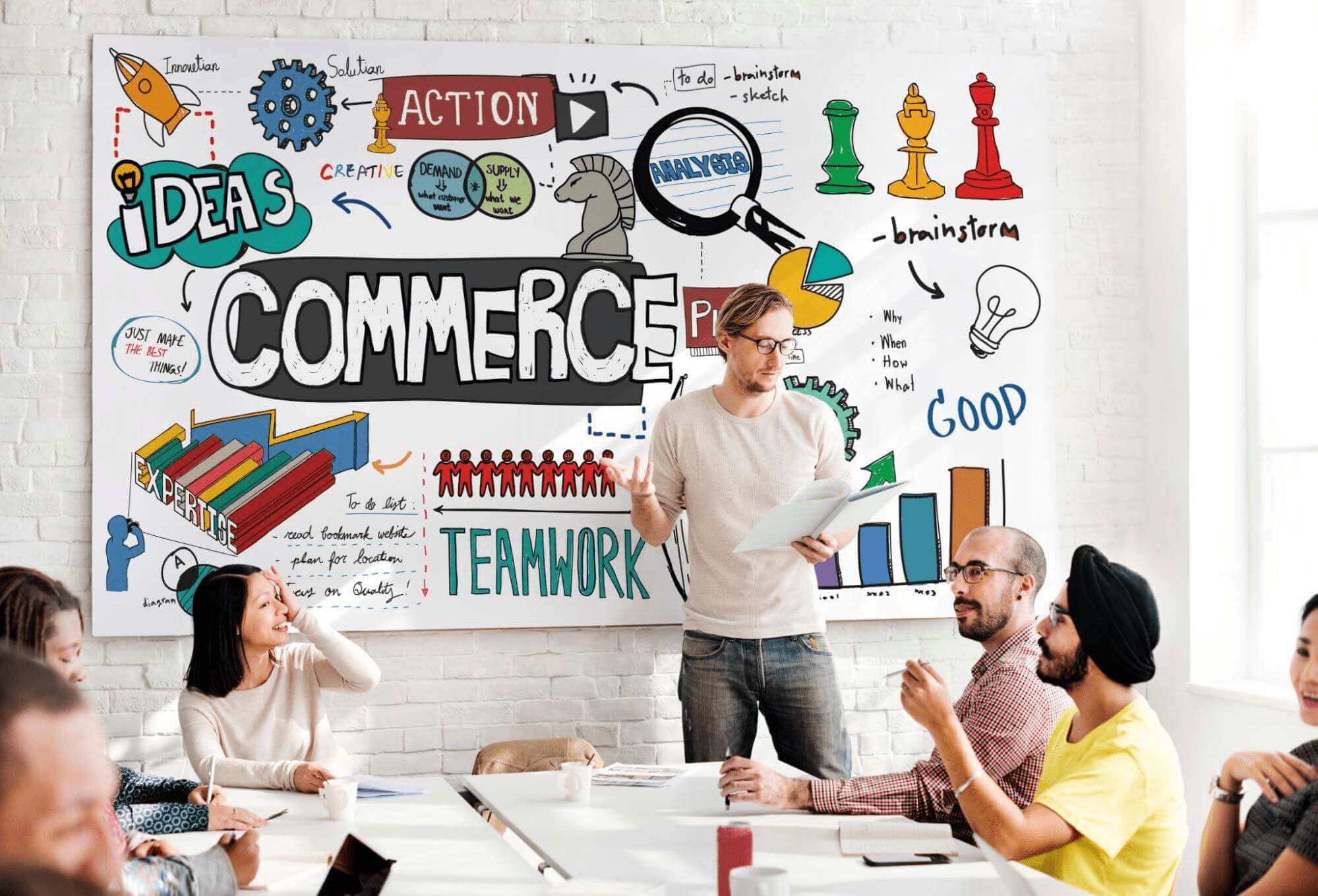 A group of people seated at a table, discussing ideas with a whiteboard displaying the word commerce