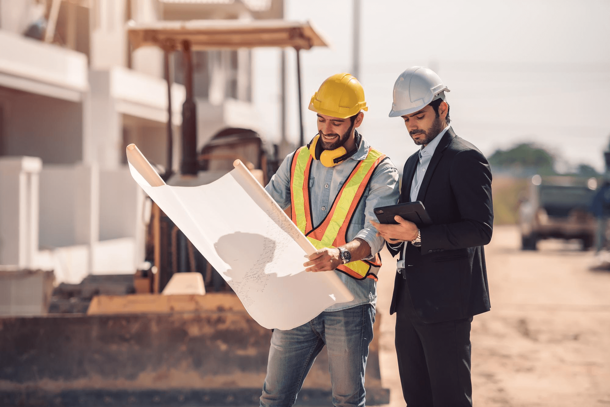 Two construction workers in hard hats and safety vests examine blueprints outdoors, conveying a professional and collaborative atmosphere on-site.