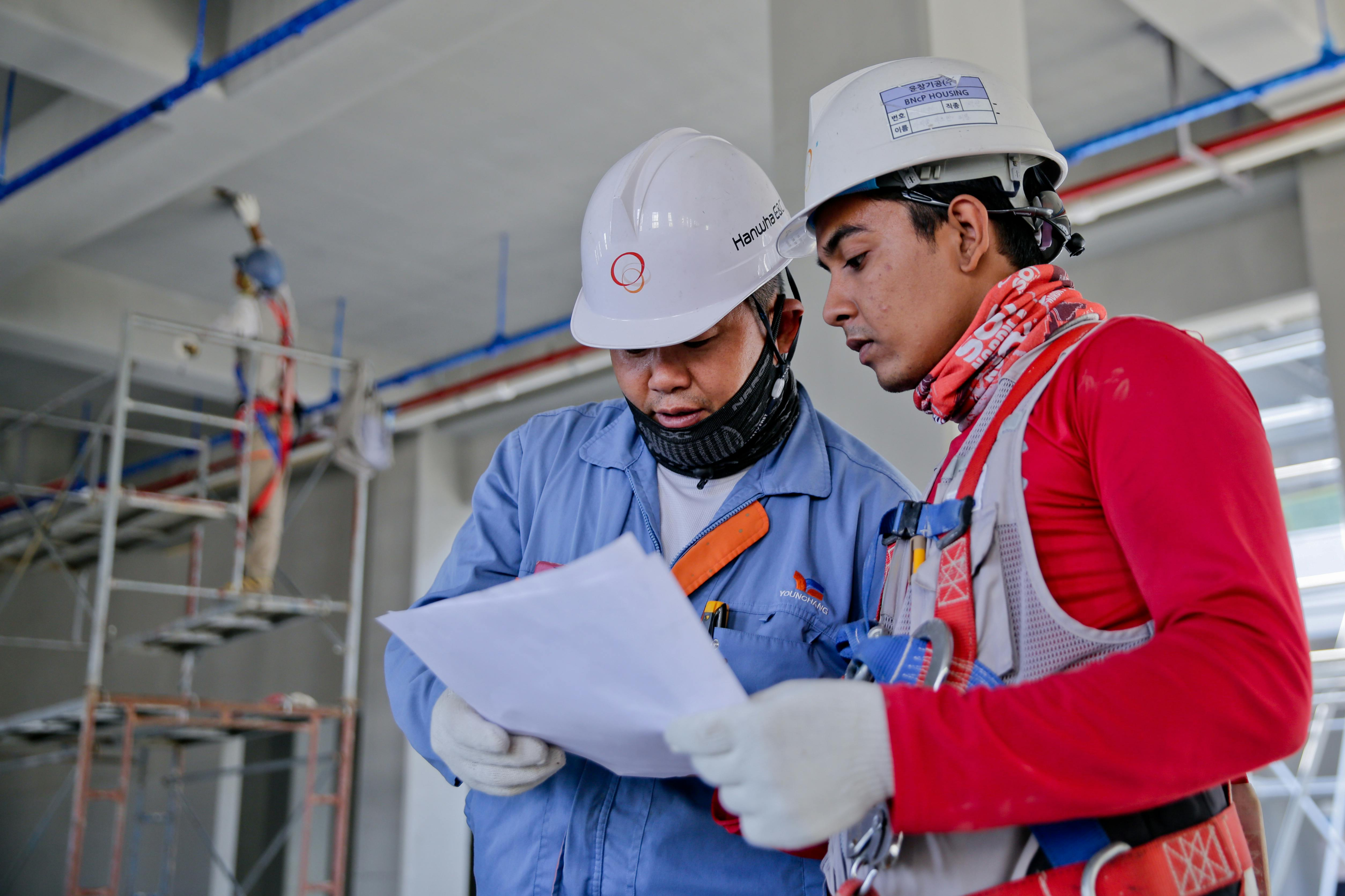 Two men in safety vests and hard hats focused on a document, possibly planning or assessing a construction project.