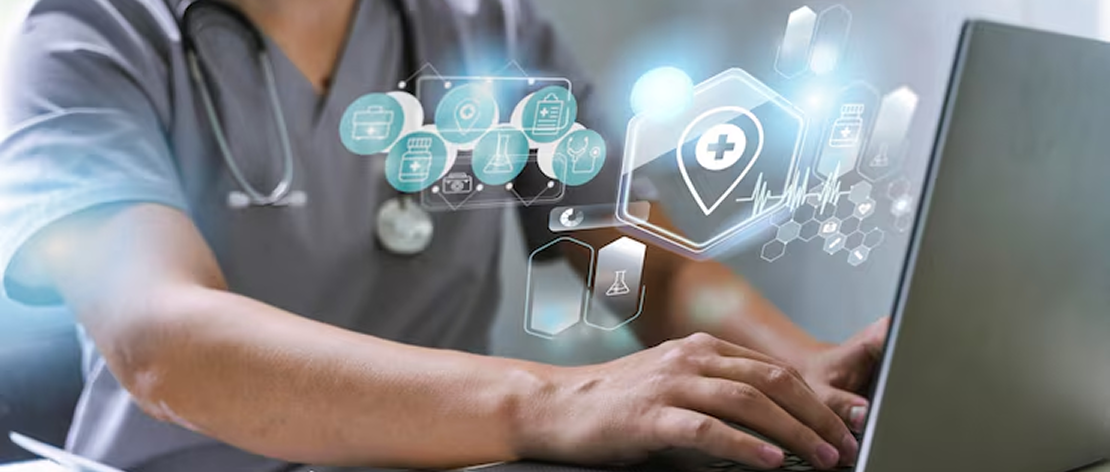 A doctor in a white coat types on a laptop displaying a medical history form. The desk holds medicine bottles, a blood pressure monitor, and medical tools.